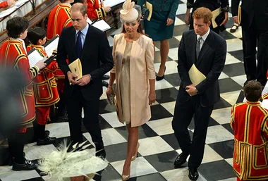 Group of elegantly dressed people in formal attire walking in a checkered floor venue.