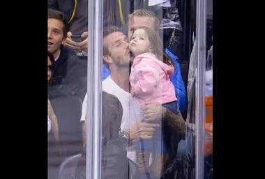 Father kisses his young daughter on the cheek at a crowded sports event, surrounded by spectators.