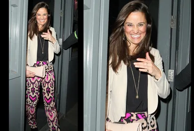 Pippa Middleton smiling and leaving a venue, wearing a black top, patterned pants, and holding a clutch.