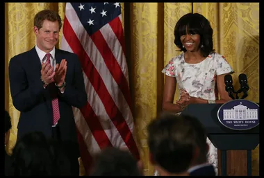 Prince Harry and Michelle Obama at a podium, with a U.S. flag backdrop, in the White House.
