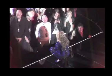 Beyoncé, in a sparkling blue outfit, performs close to the audience on stage, with fans capturing the moment.
