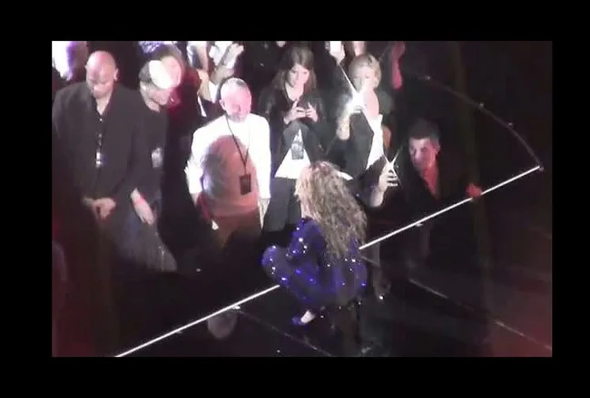 Beyoncé, in a sparkling blue outfit, performs close to the audience on stage, with fans capturing the moment.