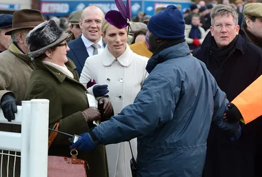 A woman in a white coat and purple hat is speaking to a security guard at a crowded outdoor event.
