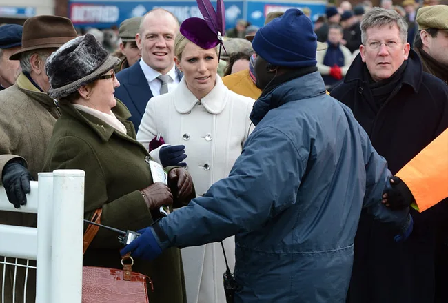A woman in a white coat and purple hat is speaking to a security guard at a crowded outdoor event.