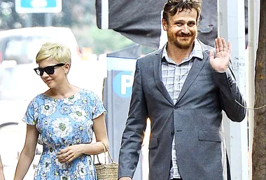 Michelle Williams and Jason Segel walking outside, Michelle in a floral dress and sunglasses, Jason in a suit waving.