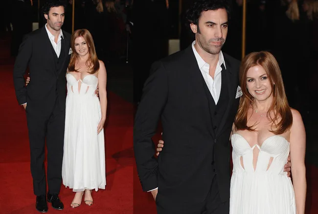 Two people posing together on a red carpet; the woman in a white dress, the man in a black suit.