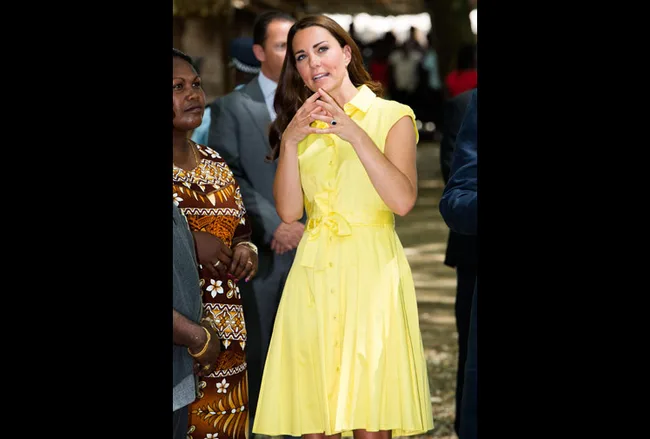 A woman in a yellow dress gestures while standing among a group outdoors.