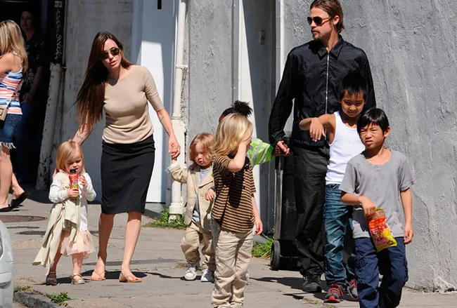 Family walking on a street in casual attire, holding hands, with children carrying snacks.