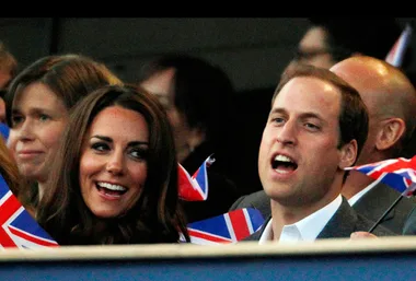 "Two people smiling and singing, holding British flags, at an outdoor event."