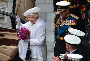 Queen Elizabeth II in a white outfit, holding flowers, with Prince Philip in naval uniform at a jubilee event.