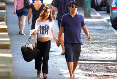 A woman showing off her baby bump and a man holding hands while walking on a sidewalk.