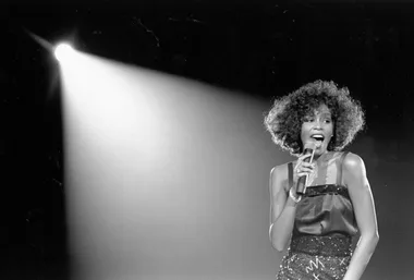 A singer performs under a spotlight, holding a microphone with a vibrant expression.