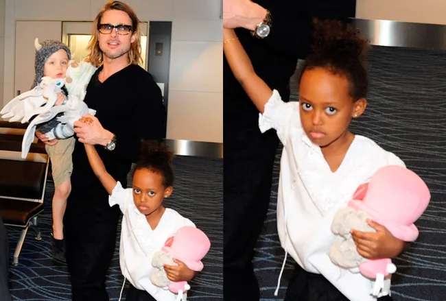 Father holding child and another young child with an ice cream toy looking serious while gripping a woman's hand at an airport.