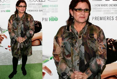 Carrie Fisher at an HBO premiere, wearing a camo-style dress and sunglasses, standing in front of a show poster.