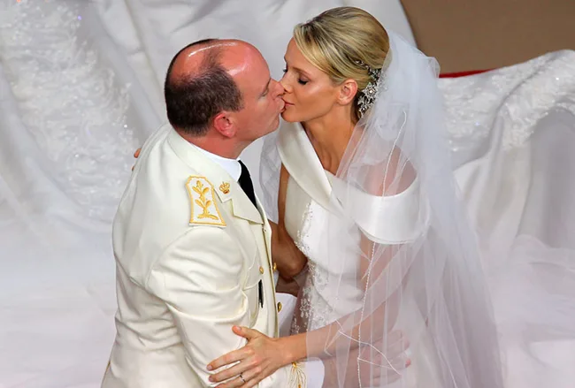 Couple in a white wedding attire sharing a kiss in an elegant ceremony setting.