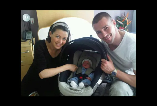 Family with a baby in a car seat, posing and smiling in a hospital room.