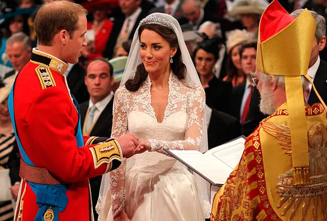 Wedding ceremony with a couple exchanging rings, attended by a priest in ornate attire, surrounded by guests.