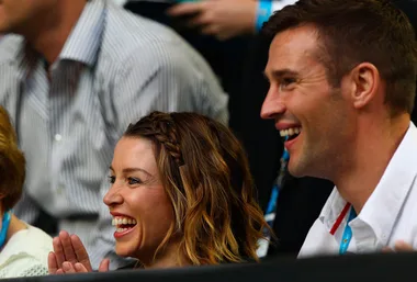 Two people smiling and clapping in an audience, wearing casual attire.
