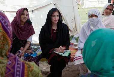 Alt text: "Angelina Jolie in a headscarf meeting with women in a Pakistani camp."