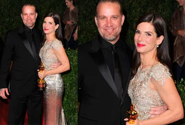 A woman in a sparkling gown holds an Oscar statuette, standing beside a man in a black suit, smiling at a formal event.