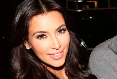 Person with long dark hair and glamorous makeup smiling warmly.