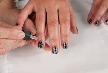 Hand applying crackle-effect black nail polish on a person's fingernails.