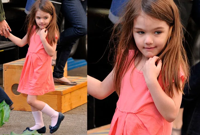 A young girl in a pink dress stands on a step and looks over her shoulder.