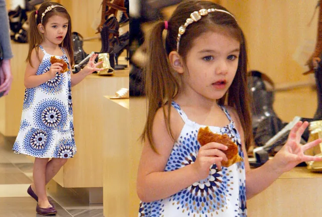 A young girl in a blue and white dress holds food while standing in a store.