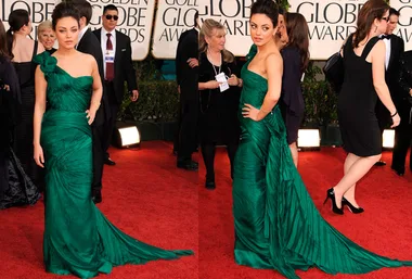 Actress in an elegant green gown poses on the red carpet at an awards event, with people and photographers in the background.