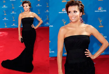 Actress in a strapless black gown with a train, on the red carpet, smiling with hand on hip, wearing statement earrings.