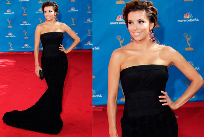 Actress in a strapless black gown with a train, on the red carpet, smiling with hand on hip, wearing statement earrings.