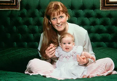 Mother and baby sitting on a green tufted couch, both smiling.