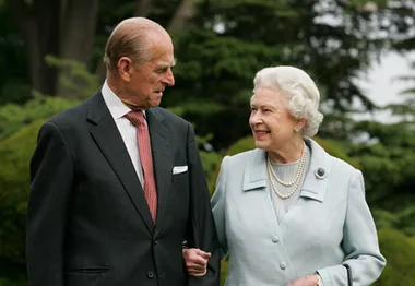 An elderly couple walking arm in arm, smiling at each other in a garden setting.