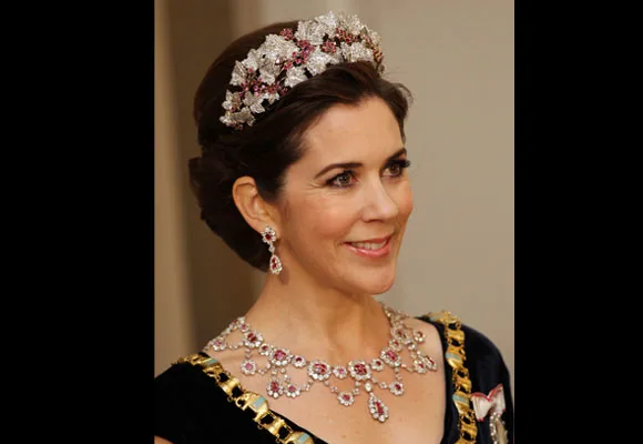 Princess in formal attire with a jeweled tiara and necklace, smiling.