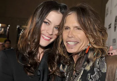 Two individuals smiling, with long hair, posing closely at an event.