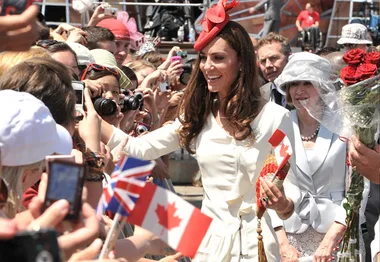 Duchess in white dress greets crowd waving British and Canadian flags during Canada tour.