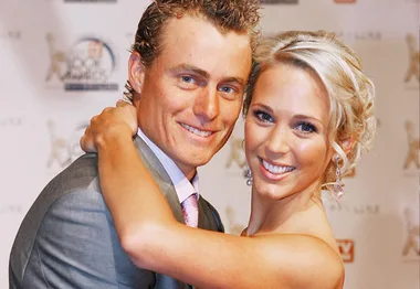 A smiling couple poses on the red carpet, the woman with blonde hair and the man in a suit.