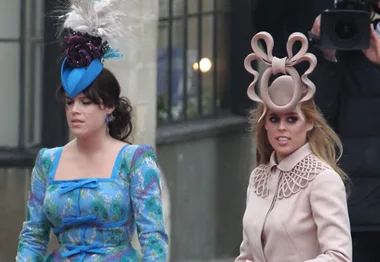 Two women walking, one in a blue floral dress with a blue hat, the other in a beige coat with an elaborate beige hat.