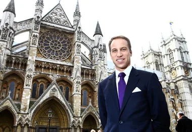 Man in a suit stands in front of a historic cathedral with intricate Gothic architecture and a large rose window.
