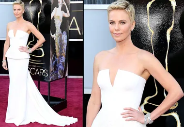 Person in elegant white gown poses on red carpet at an awards event, with sleek hairstyle and bold makeup.