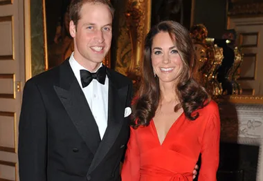 A couple in formal attire at a glamorous event, with a woman in a red dress and a man in a black tuxedo smiling together.