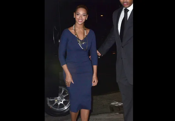 A woman in a blue dress and necklace smiles while walking outside at night, accompanied by a person in a suit.