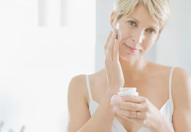 A woman applying face cream in a bright bathroom.