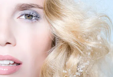 A woman with blonde hair, winter makeup, and snowflakes in her hair, showcasing a winter beauty look.