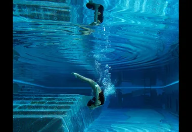 Diver performing a graceful underwater flip in a serene, clear blue spa pool.
