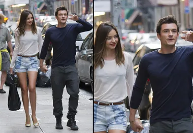 Young couple holding hands walking in the city, both casually dressed, with cars and city buildings in the background.