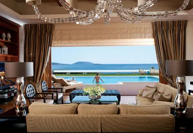 Luxurious hotel suite with ocean view, pool, elegant decor, and chandelier, featuring a person swimming.