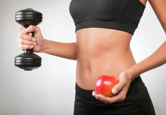 Person holding a dumbbell in one hand and a red apple in the other, wearing black workout attire.