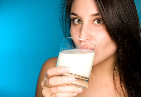 Woman drinking a glass of milk with a blue background.