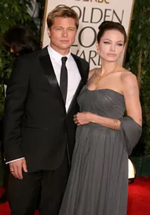 A couple in formal attire at the Golden Globe Awards, standing on a red carpet with greenery in the background.